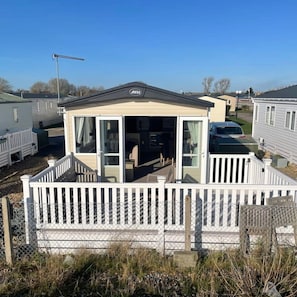 A mobile home with a covered porch, white railings, and a visible logo on the roof. - 74 Bayside Cove Pevensey Bay Holiday Park (Pevensey)