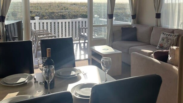 A room with a dining table set for two, a sofa, and a balcony with a view of the city.