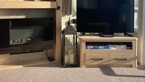 A living room with a fireplace, a television on a wooden stand, and a window with curtains.