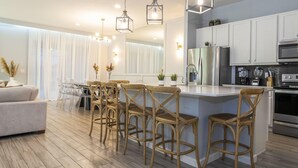 A modern kitchen with a central island, bar stools, stainless steel appliances, and a dining area with a sofa and chairs. - Wonderful 12b11 5bath Bella Vida Resort (Kissimmee)