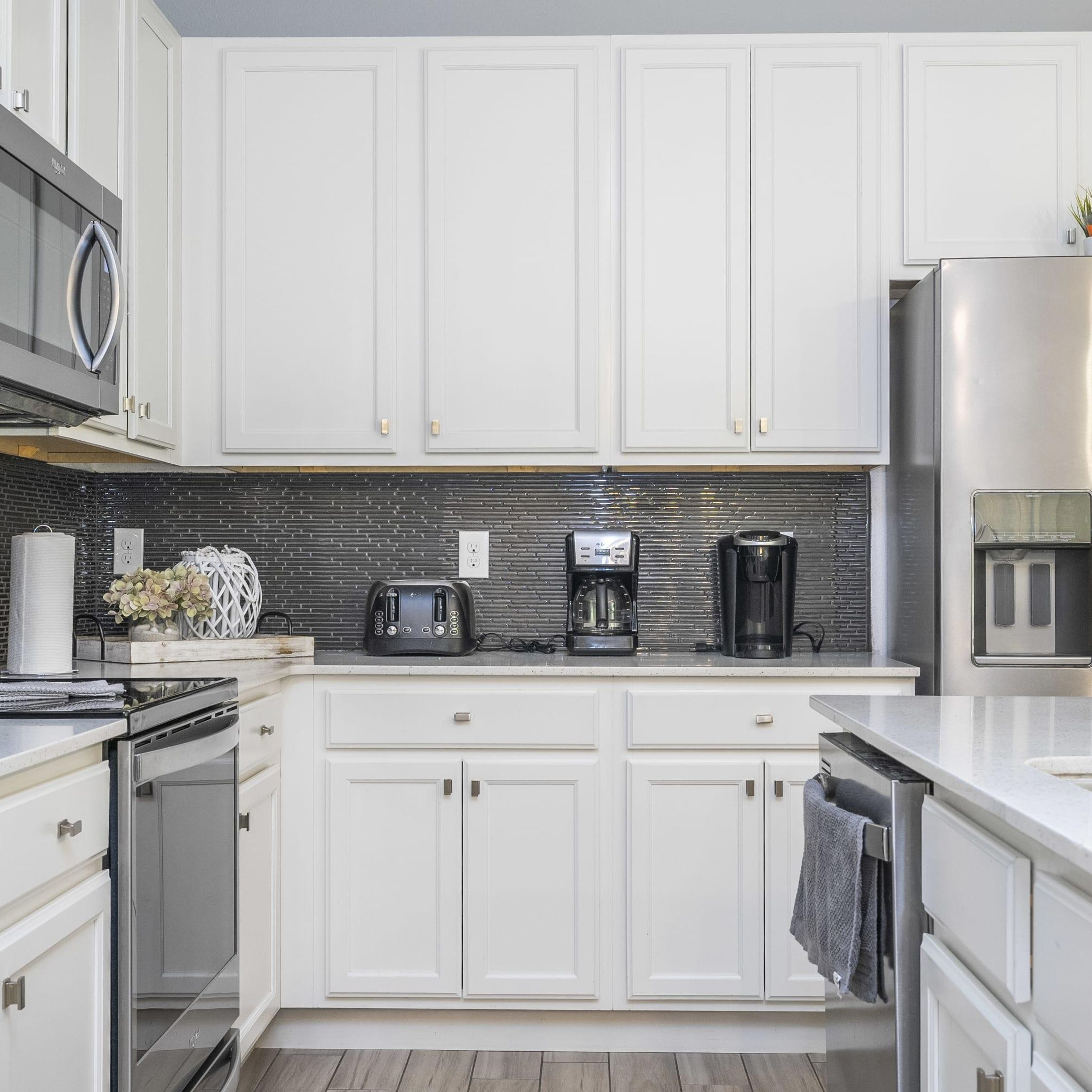 A modern kitchen with white cabinets, a stainless steel refrigerator, a coffee maker, and a toaster.