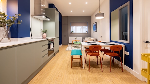Una cocina moderna con armarios grises, una mesa de comedor con sillas naranjas y una ventana con persianas.