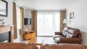 A living room with a brown leather sofa, a wooden coffee table, and a television on a stand. - Ferncourt Stepaside (Dublin)