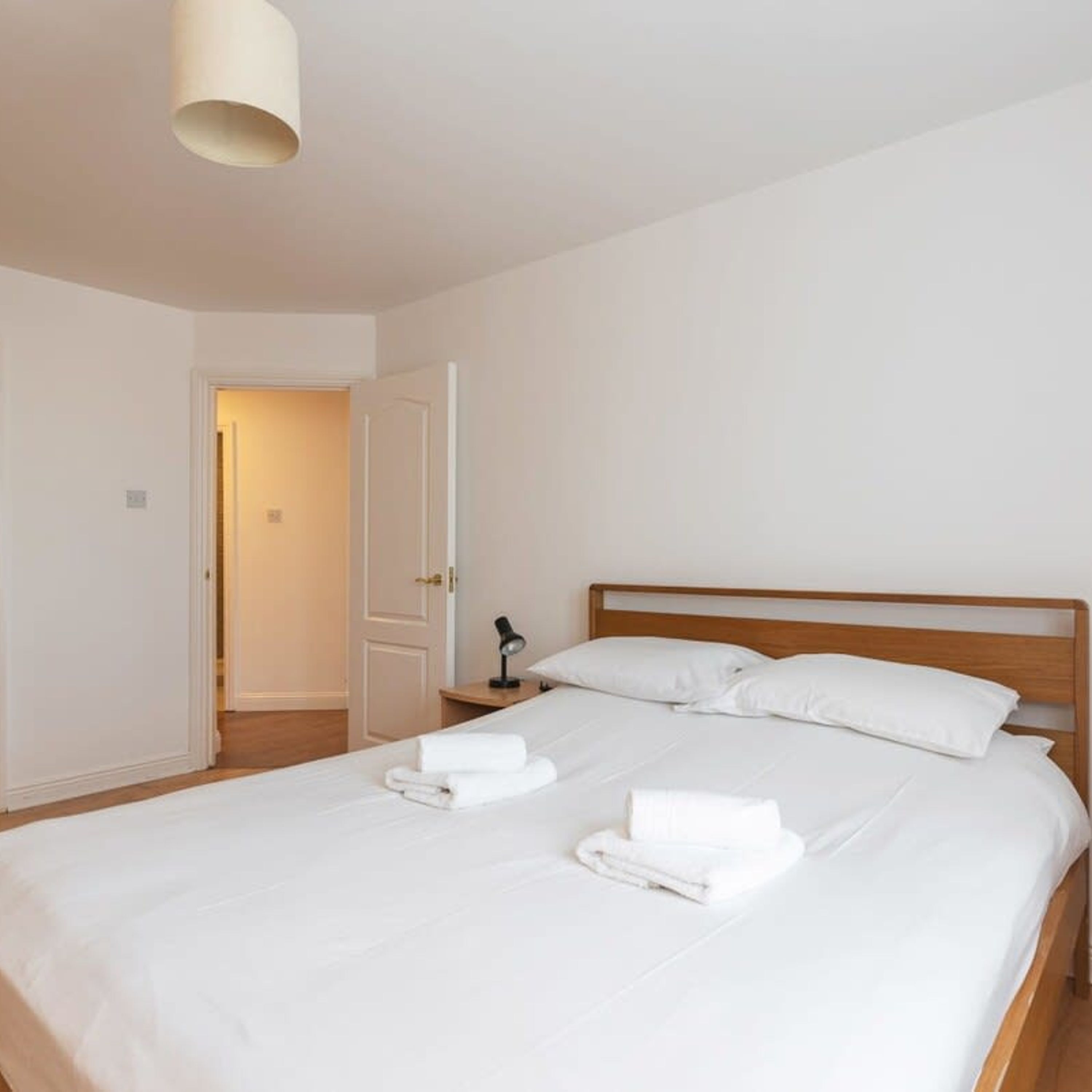 A neatly made bed with white linens and towels, a wooden headboard, and a bedside lamp.