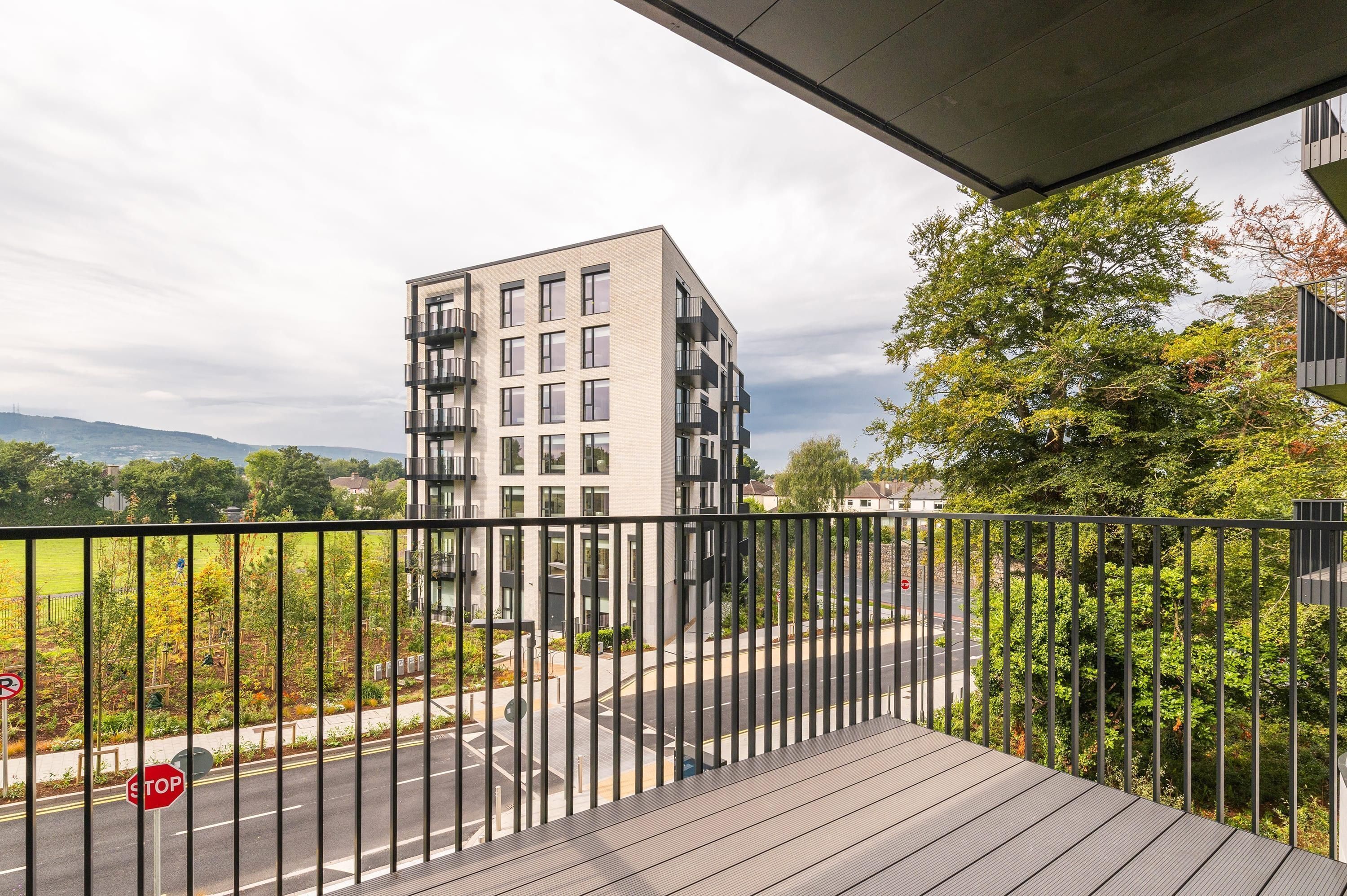 A modern building with multiple balconies and a view of a road and greenery.