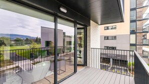 Een balkon met uitzicht op een groen park, een glazen deur en een gebouw met het bord 'The Orange City Hotel'.