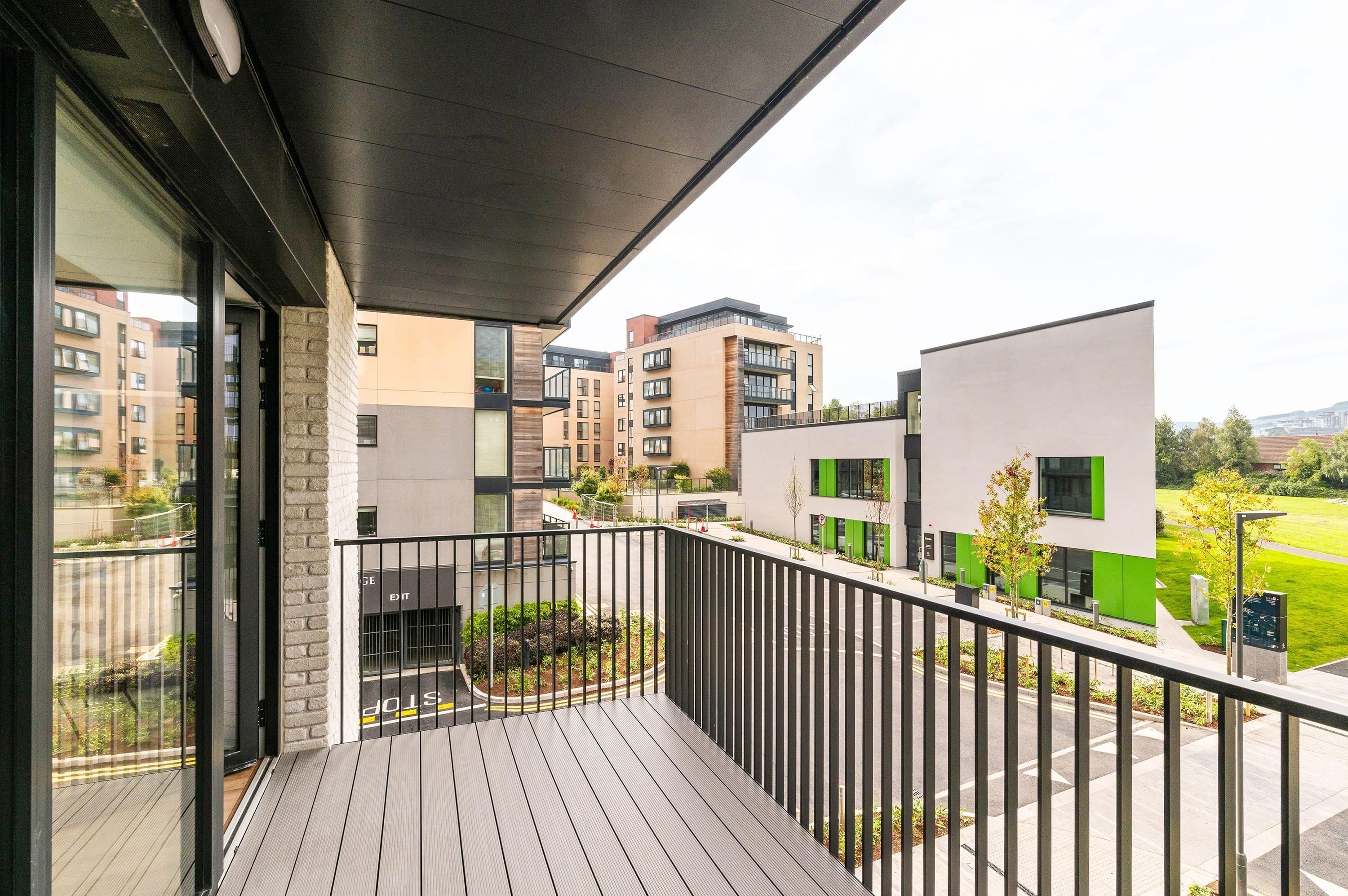 Un balcón con vistas a edificios modernos, una terraza de madera y una barandilla de metal.