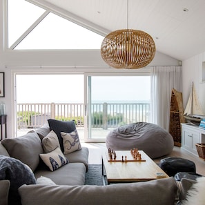 Uma sala de estar moderna com uma janela ampla, uma luminária pendente trançada, um sofá, um bean bag e um tabuleiro de xadrez.