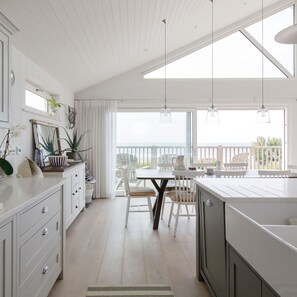 A modern kitchen with white cabinetry, a dining area with a table and chairs, and a balcony with a view. - Hamptons Style Lux Beach House (Chichester)