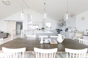 Uma cozinha ampla com armários brancos, uma mesa de jantar de madeira e luminárias pendentes.