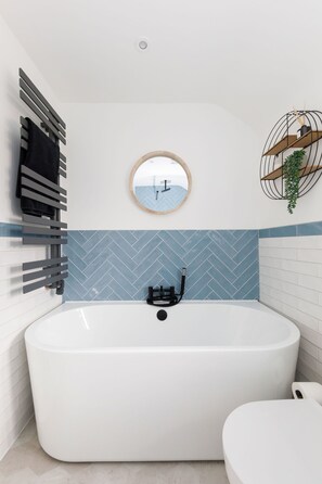 A modern bathroom with a freestanding bathtub, a toilet, a towel rack, a mirror, and a potted plant. - Renovated Home for 8 Canal Walk to Chichester (Chichester)