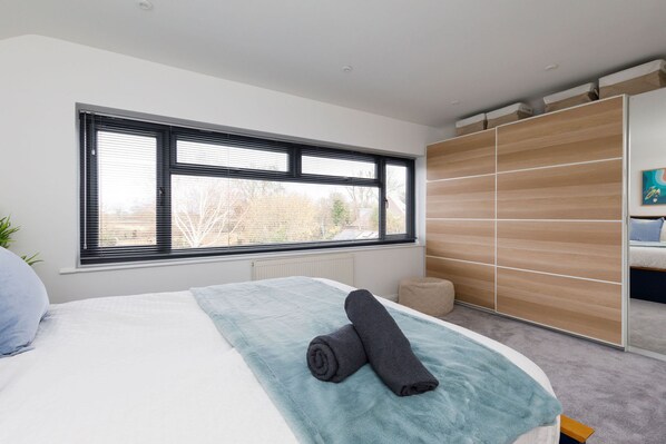 A bedroom with a large window, a bed with a blue blanket, and a wooden wardrobe. - Renovated Home for 8 Canal Walk to Chichester (Chichester)