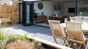 Eine Terrasse mit Esstisch und Stühlen, eine Glastür zum Verschieben und ein kleiner Garten mit Pflanzen.