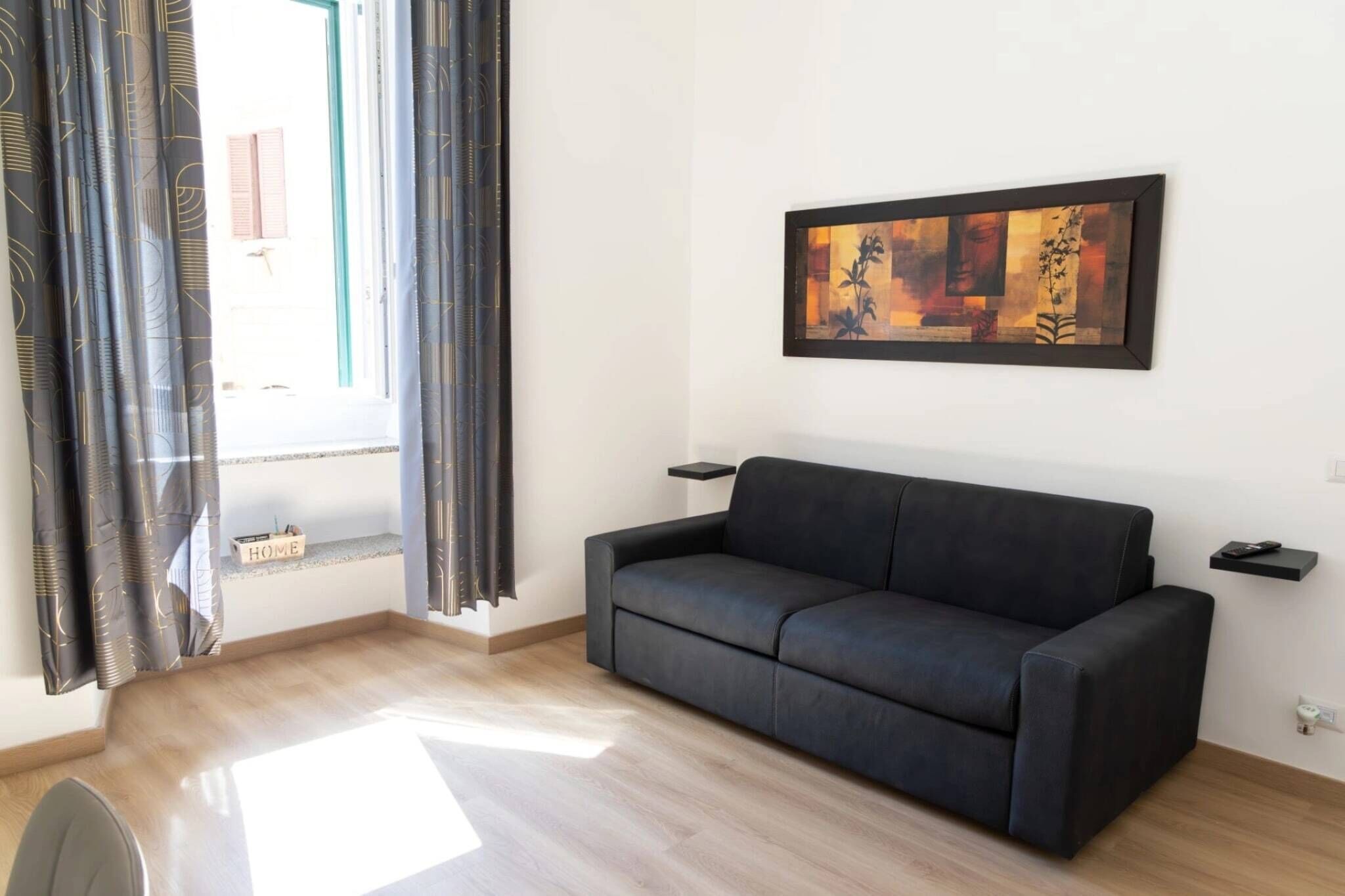 Ein modernes Wohnzimmer mit einer schwarzen Couch, einem gerahmten abstrakten Gemälde und einem Fenster mit Vorhängen.