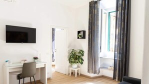 Un salon moderne avec un téléviseur à écran plat, un bureau, une chaise, une plante en pot et un canapé.