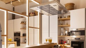 Una cocina moderna con armarios blancos, una campana extractora de acero inoxidable y una barra desayunadora con cuencos de fruta.