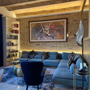 A modern living room with a sectional sofa, a blue armchair, a coffee table, and a bookshelf against a brick wall. - The Avenue 2BR Luxury Unit in Diagonal Ave (Barcelona)