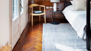 Une chambre à coucher avec un lit à baldaquin, une chaise en bois, une petite table avec une lampe et une grande fenêtre.