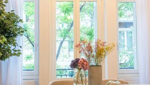 Ein Essbereich mit einem runden Tisch, Stühlen, einer Blumenvase und Blick auf Grün durch große Fenster.
