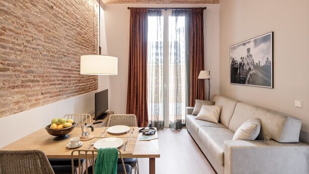 A cozy living room with a brick wall, a dining area with a table set for two, and a sofa. - Pau Claris Double Home Next to Paseo de Gracia (Barcelona)