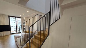 A modern apartment with a wooden staircase, a living area with a sofa, and a large window offering a city view. - The Roger Terrace 2BR With Pool gym in Barcelona (Barcelona)