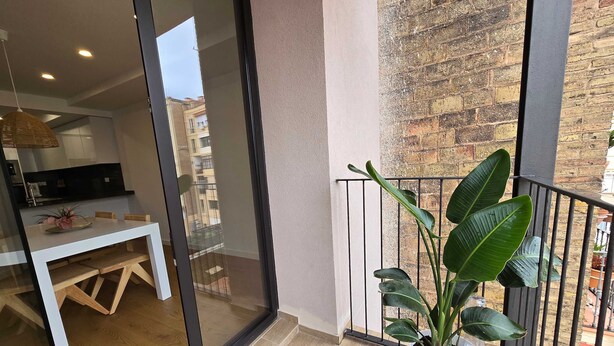 A balcony with a potted plant, a dining area with a table and chairs, and a view of a brick building. - The Roger Terrace 2BR With Pool gym in Barcelona (Barcelona)
