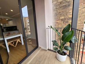 A balcony with a potted plant, a dining area with a table and chairs, and a view of a brick building. - The Roger Terrace 2BR With Pool gym in Barcelona (Barcelona)