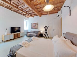 A modern bedroom with a wooden ceiling, a large bed, a TV, a sofa, and a lamp. - 4bnb - Luxury Navona Apartment (Rome)