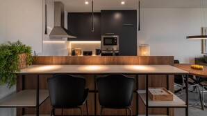 Una cucina moderna con mobili scuri, un'isola centrale con due sedie nere e un forno a microonde.