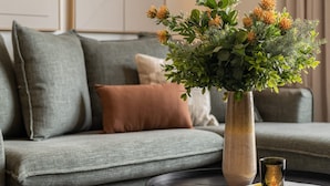 Un soggiorno con un divano grigio, un tavolino da caffè nero rotondo e un vaso con verde fogliame e fiori arancioni.