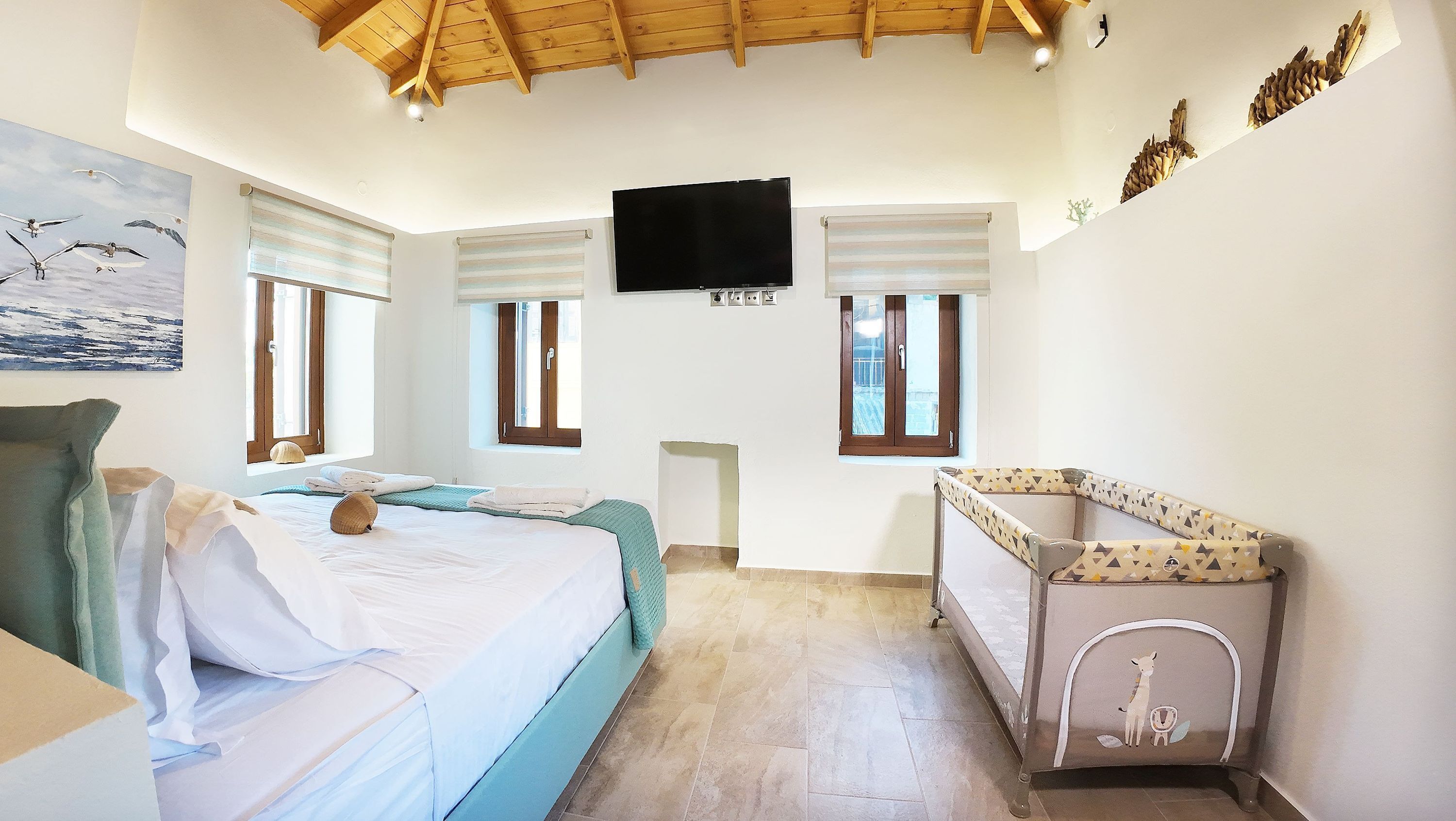 A bedroom with a bed, a small table, a TV, and windows with blinds.