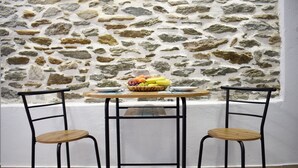 Una habitación con pared de piedra, una mesa redonda de madera, dos sillas de metal y una cesta de frutas sobre la mesa.