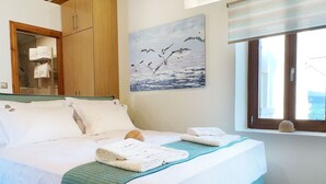 Un dormitorio con cama, vigas de techo de madera, un cuadro de pájaros, una ventana con vistas y suelo de baldosas.