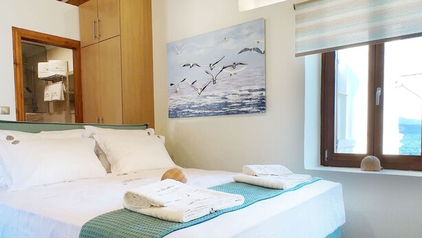 Un dormitorio con cama, vigas de techo de madera, un cuadro de pájaros, una ventana con vistas y suelo de baldosas.