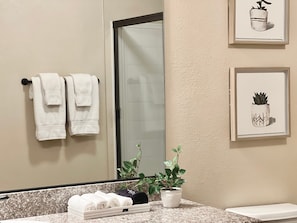 A bathroom with a mirror, two towels on a rack, a potted plant, and two framed pictures on the wall. - Relaxing 2-br Apt With Pool Hot Tub Gym and Basketball Court Access (Reno)