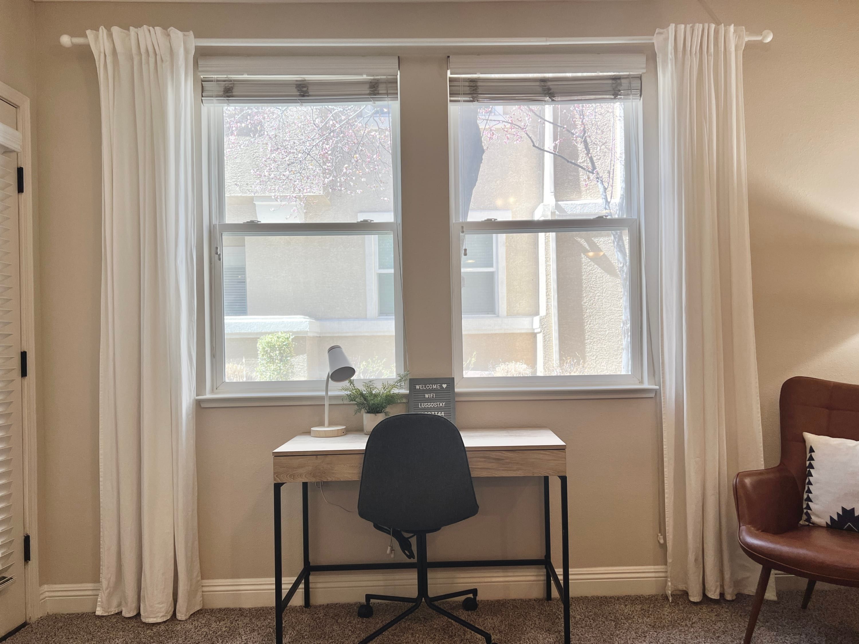A room with a desk, chair, and a window with curtains.