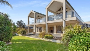 A modern two-story house with a balcony, surrounded by well-maintained lawns and tropical plants. - Sunset View Luxury 4 Bedrooms With Sauna (Mount Martha)