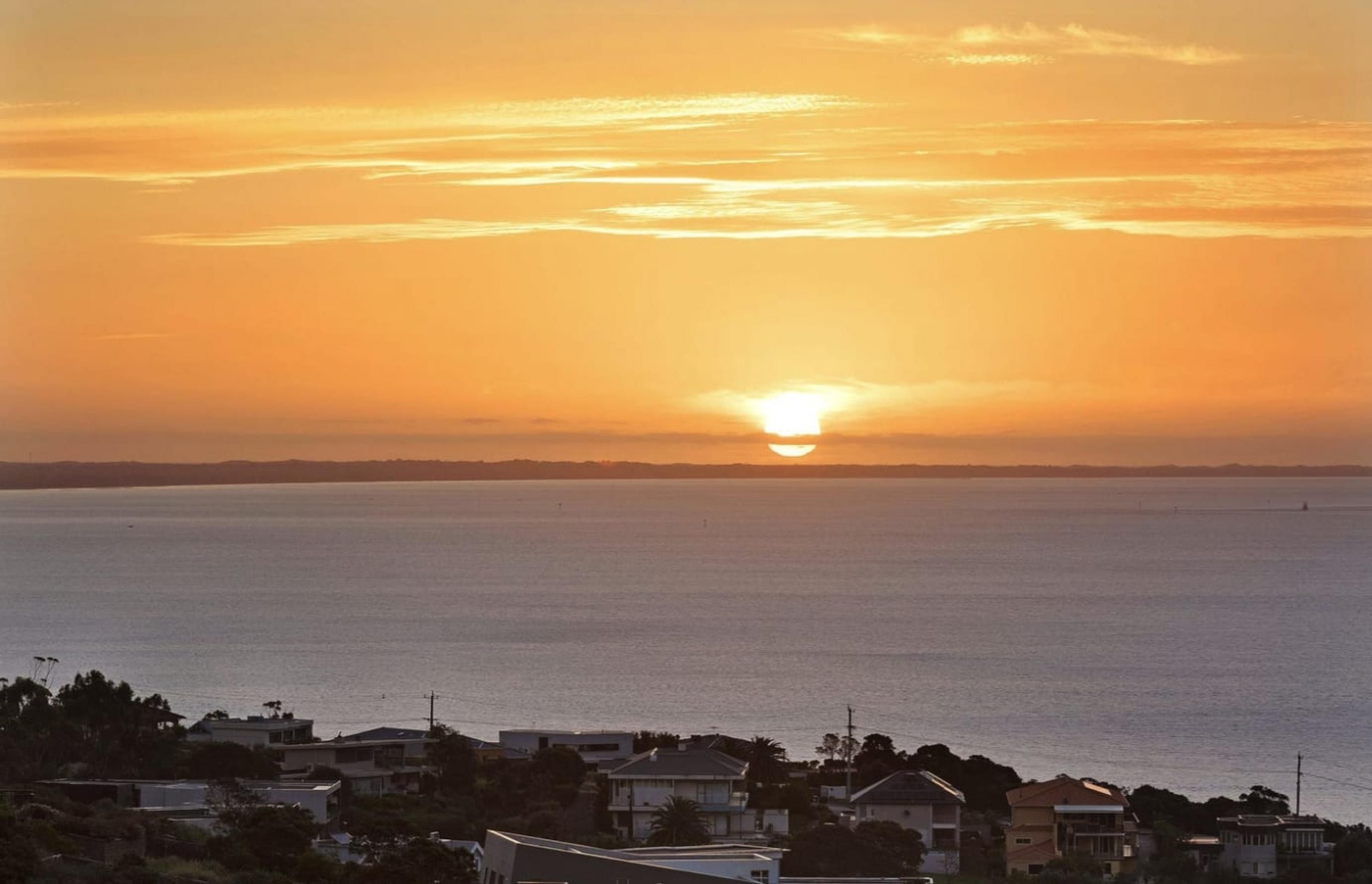 A coastal sunset view with a calm sea and a row of houses in the foreground.