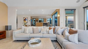 A modern living room with a large L-shaped sofa, a coffee table, and a kitchen in the background. - Sunset View Luxury 4 Bedrooms With Sauna (Mount Martha)