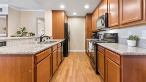 A modern kitchen with wooden cabinets, granite countertops, a black refrigerator, a microwave, and a stove.