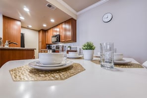 A modern kitchen with wooden cabinets, a refrigerator, and a microwave. There is a dining table set with plates, bowls, and glasses. - 2BR Getaway Pool Gym Basketball Court Theater Access (Reno)