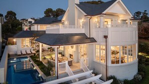 Una casa grande de dos pisos con piscina, mobiliario exterior y un interior bien iluminado.