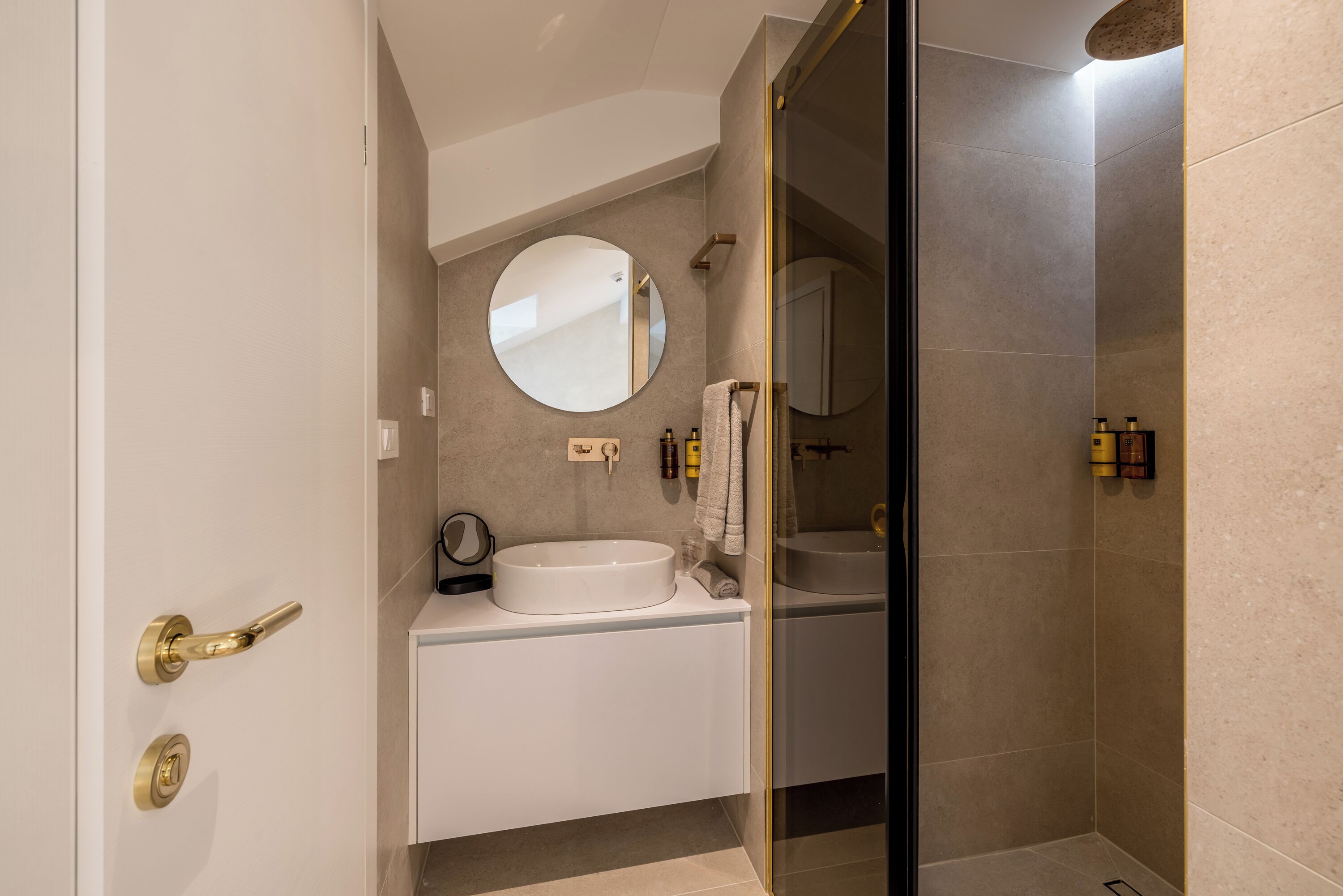 Un baño moderno con un espejo redondo, dos lavamanos y una ducha con mampara de vidrio.