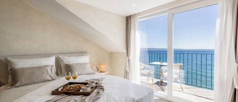 Ein Schlafzimmer mit einem großen Bett, einem Frühstücksbrett und einem Balkon mit Meerblick.
