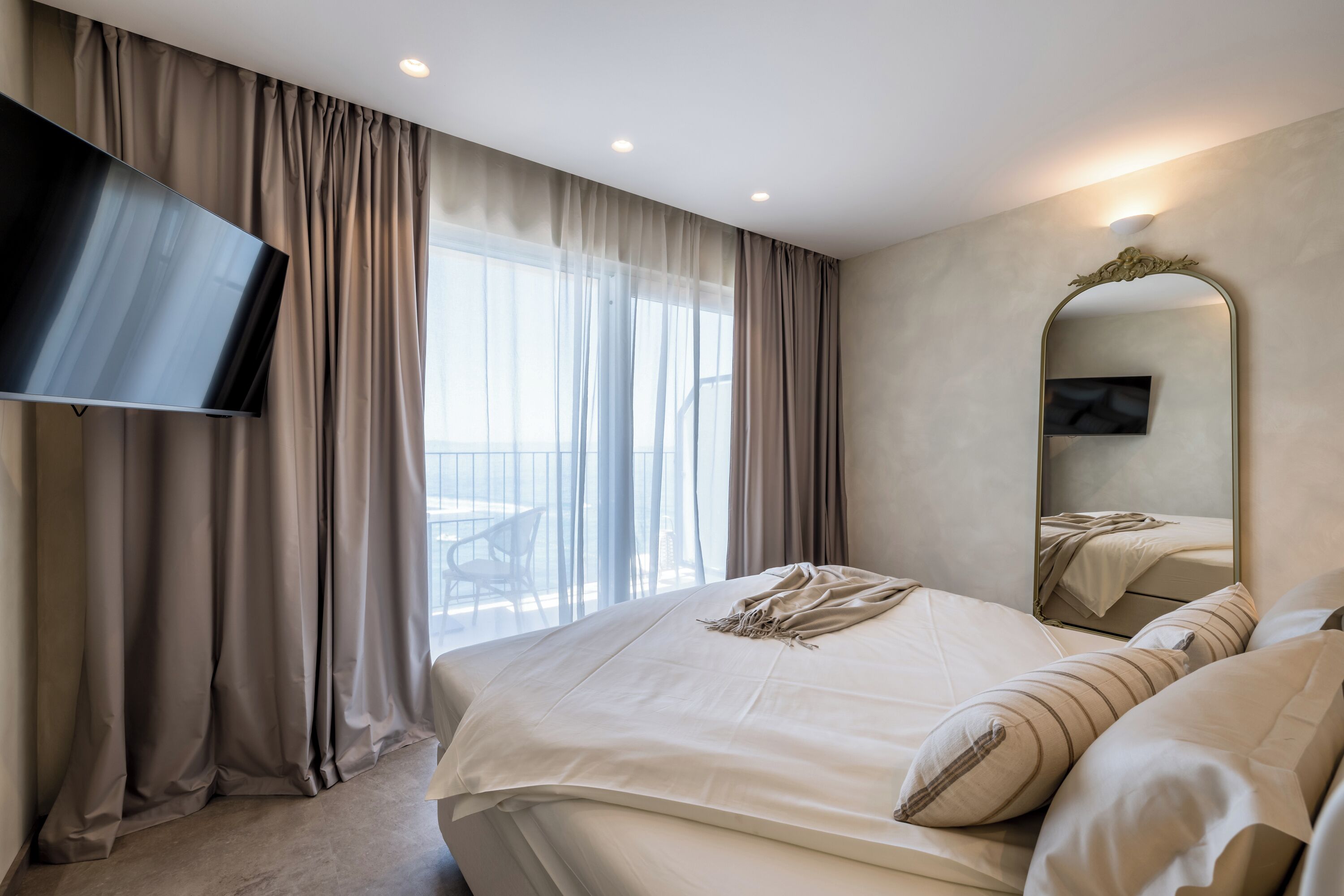 Habitación de hotel con una cama grande, televisión de pantalla plana, un espejo y vistas al balcón.