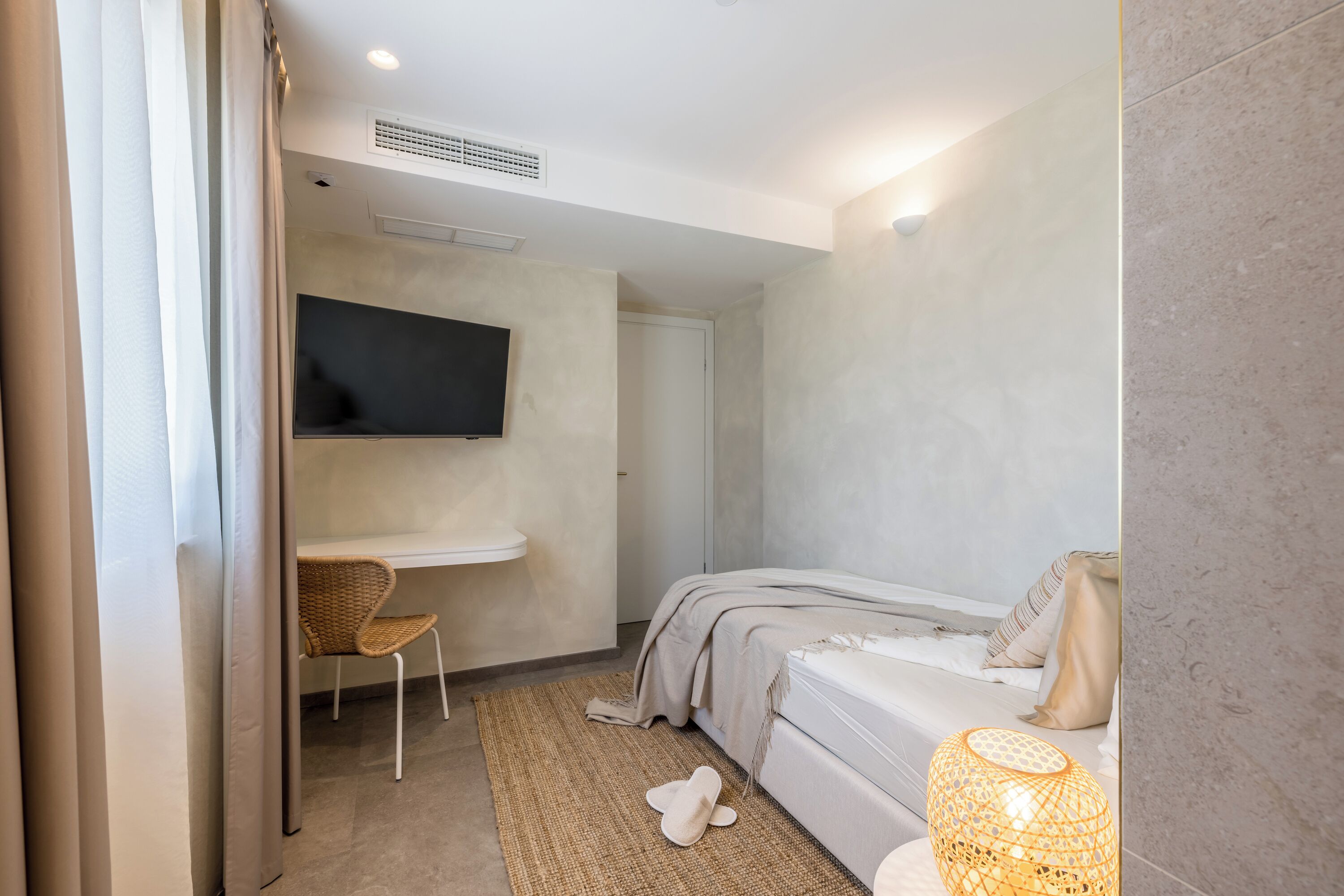 A modern bedroom with a bed, a desk, and a television.