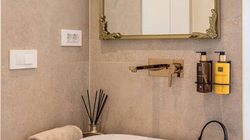 Et badeværelse med en rund vask, et spejl med en detaljeret ramme, et håndklæde og to flasker shampoo.
