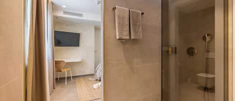 A modern bathroom with a glass-enclosed shower, a towel rack with two towels, a chair, and a small table with toiletries.