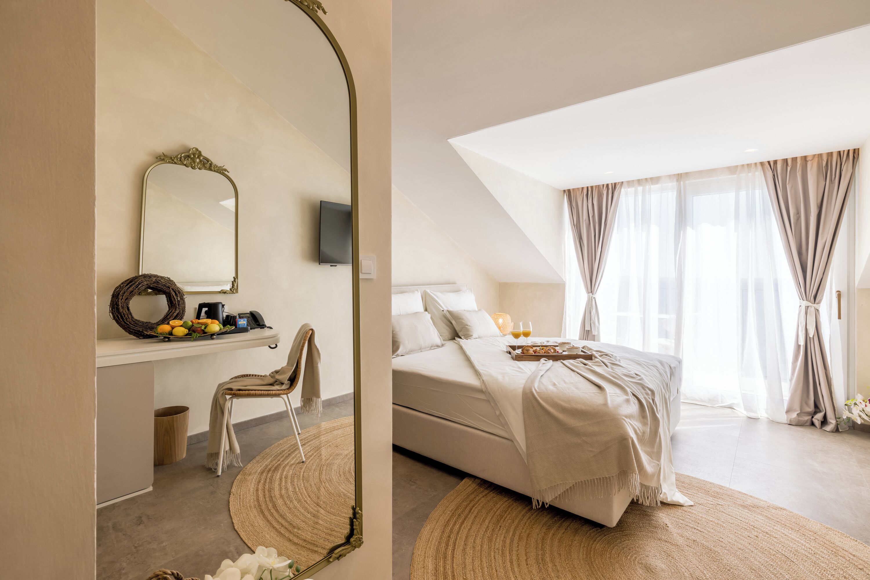 A bedroom with a bed, a bedside table with a lamp, a mirror, and a window with curtains.