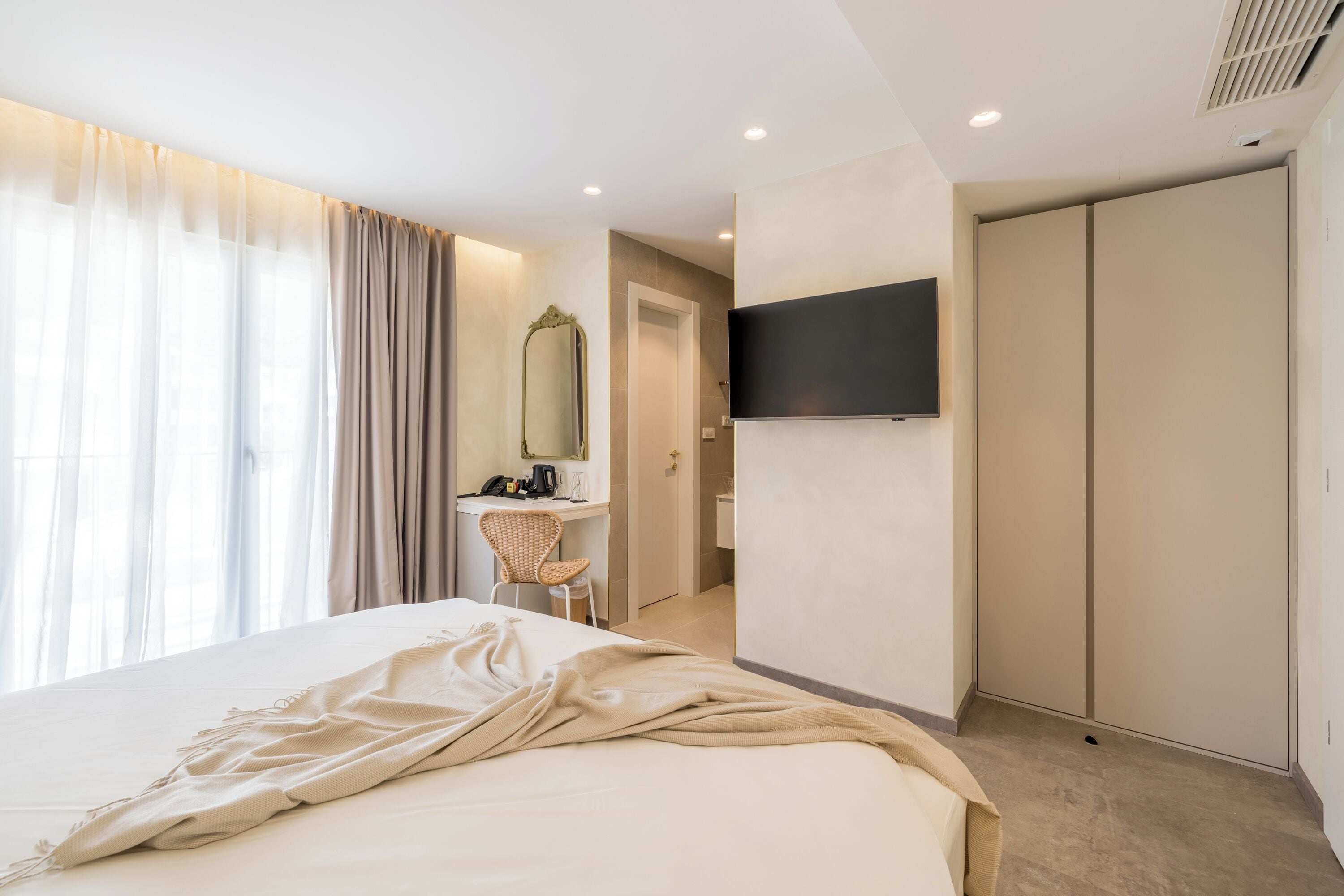 A hotel room with a large bed, a desk with a chair, a television mounted on the wall, and a wardrobe.